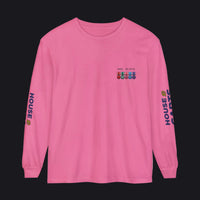 A pink long-sleeve crewneck t-shirt with a small multicolor graphic on the left chest and 'HOUSE OF CARDS' printed vertically in blue on both sleeves, shown against a plain white background.