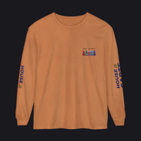 A long-sleeve crewneck t-shirt in a warm burnt orange color, featuring a small multicolor military ribbon graphic and 'MAY 21 RTO' printed on the left chest, with 'HOUSE CARDS' printed vertically in blue on both sleeves.