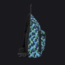 A side-profile view of a sling backpack featuring a blue, green, and navy puzzle-piece camouflage pattern, with black straps and zippers, set against a plain white background.