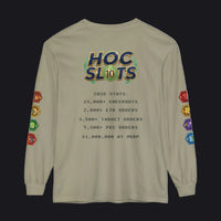 A beige long-sleeve t-shirt with a detailed graphic on the back. The graphic features a colorful 'HOC SLOTS 10' logo at the top, followed by pixel-style text detailing game statistics (including '2026 STATS' and '$1,000,000 AT MSRP').
