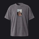 A dark gray mineral-wash short-sleeve t-shirt with a central graphic print of a hand holding a phone, displayed against a solid light gray background.