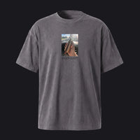 A dark gray mineral-wash short-sleeve t-shirt with a central graphic print of a hand holding a phone, displayed against a solid light gray background.