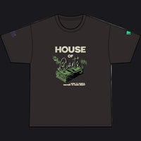 A black short-sleeve t-shirt with a graphic on the front reading 'HOUSE OF Cards' in beige and green, featuring an illustration of a stack of cash and roses. The shirt is displayed flat against a solid white background.